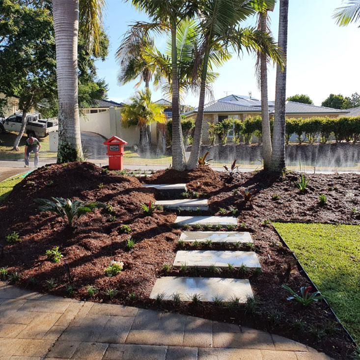 Image is circle shaped and contains a photo of landscaping underway with paver steps leading through garden